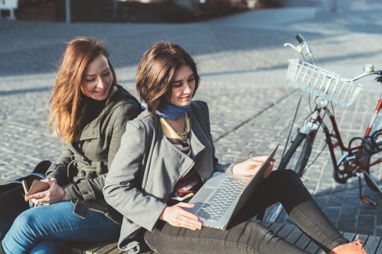 two young women sitting outdoor using notebook